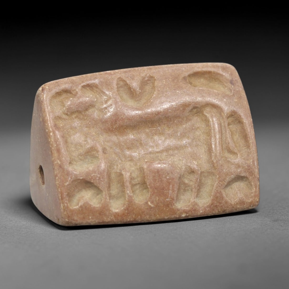 Ancient Triangular Cylinder Seal - Near Eastern Zoomorphic Artifact, 12ZR: This artifact is a triangular stone cylinder seal, executed in the classic glyptic tradition of the ancient Near East. The face features a reclining zoomorphic figure (likely a bovine or equine) surro