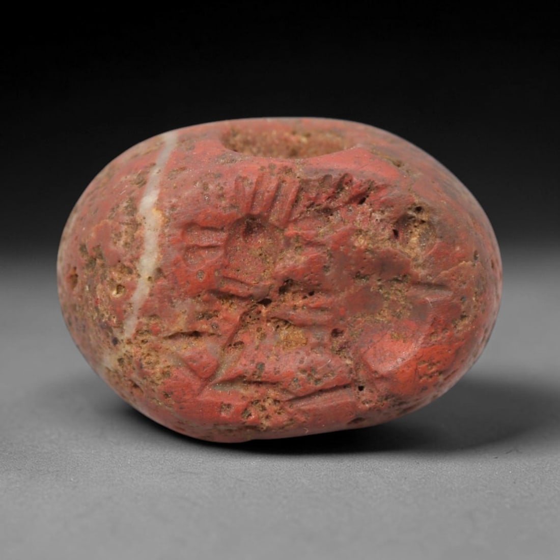 Ancient Stone Hemispherical Stamp Seal - Near Eastern Animal Figure, 86ZS: Crafted from dense, reddish stone with a distinct white mineral inclusion, this hemispherical stamp seal bears incised carving of a stylized animal figure, likely a bovid or ibex, with linear body det