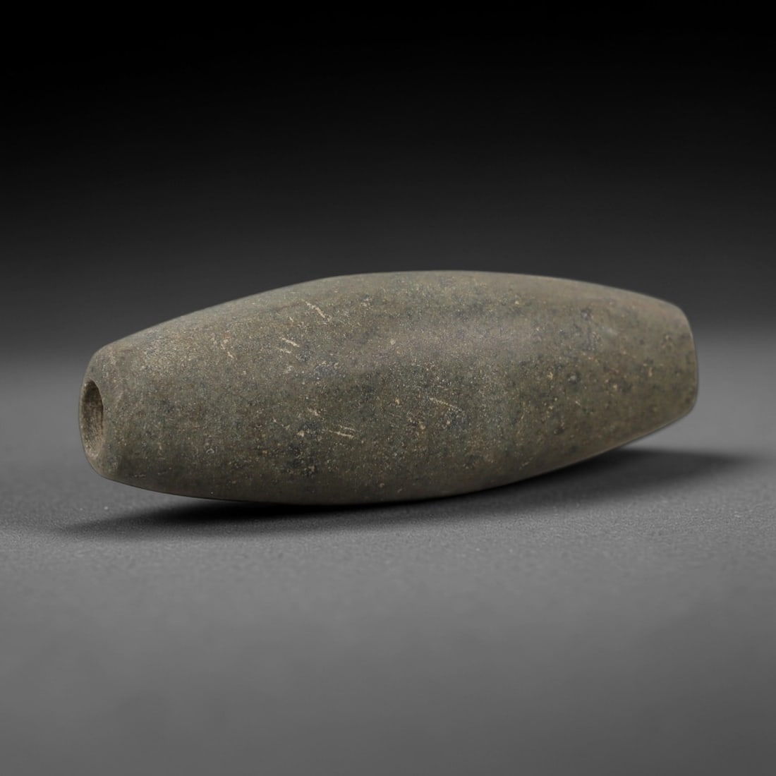 Ancient Egyptian Stone Bead - Cylindrical Carved Ornament, 62AE: Carved from stone, this ancient Egyptian cylindrical bead features subtle linear carvings and natural veining, typical of Late Period beadwork. The compact form has a central perforation, indicating i
