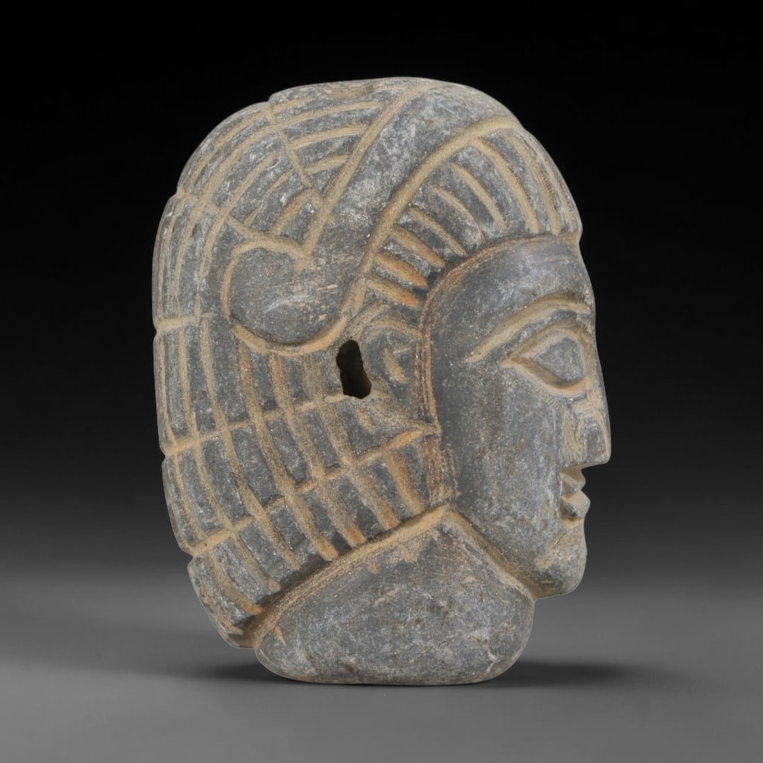 Ancient Stone Amulet - Near Eastern Bust Plaque Pendant, 64FY: Carved from dark stone, the amulet is a profile bust plaque crafted in the ancient Near Eastern style, featuring a raised relief portrait of a human head. The surface bears incised details rendering a