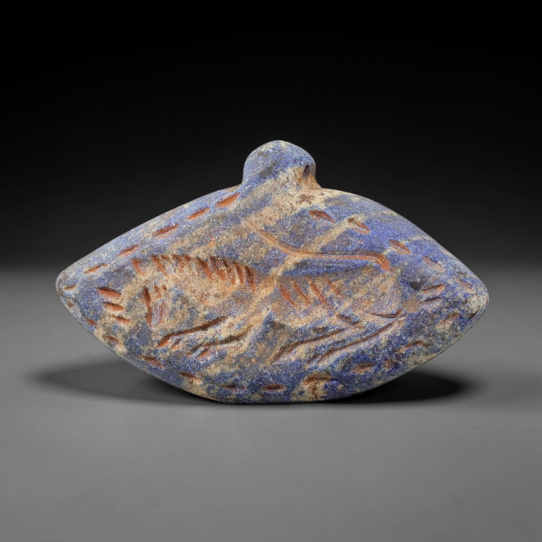 Ancient Lapis Lazuli Amulet - Near Eastern Animal Figurine, 1BA: Carved from lapis lazuli, the amulet takes an oval, eye-shaped form with a suspension loop at the top, designed for wear as a protective talisman. The front face is incised with a stylized quadruped a