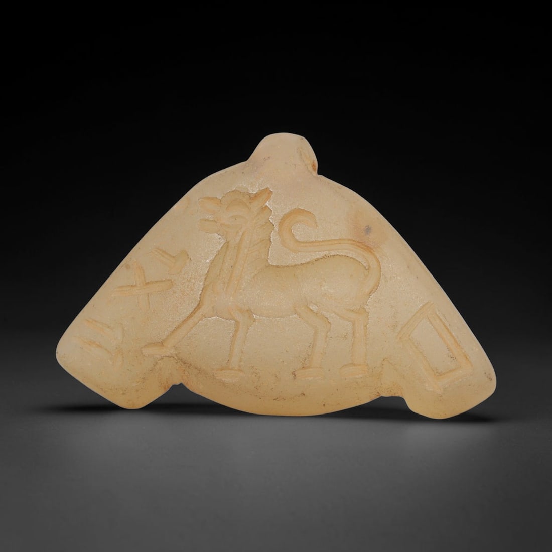 Ancient Chalcedony Amulet - Near Eastern Animal Figure, 40ZX: Carved from translucent chalcedony, this amulet features a relief depiction of a stylized quadrupedal animal, likely a mythical or equine creature, rendered with incised details defining its form, man