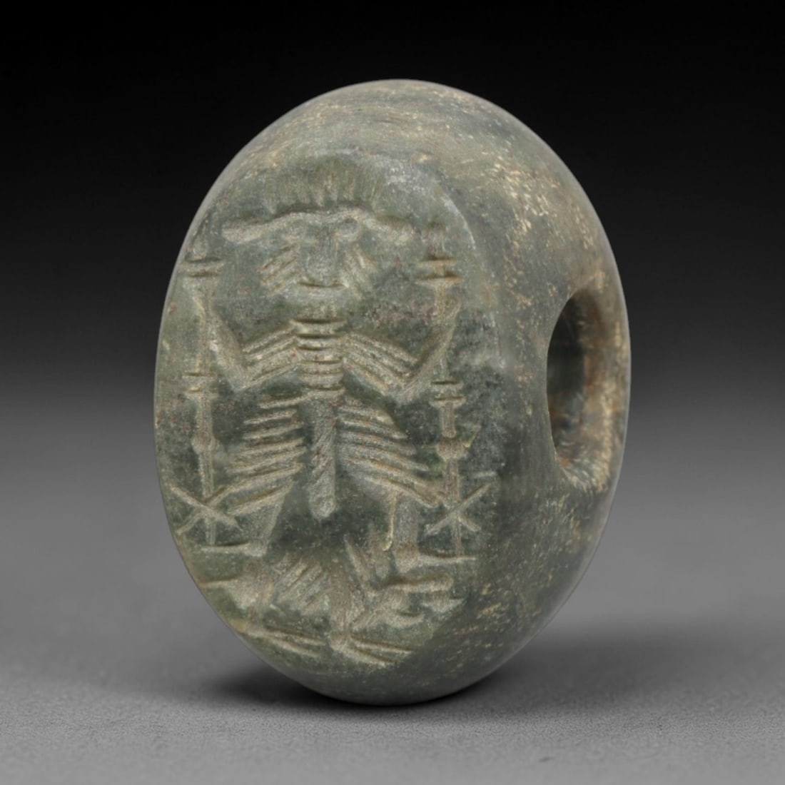 Ancient Stone Hemispherical Stamp Seal - Near Eastern Deity Figure, 37ZP: Crafted from a fine-grained, greenish stone, this hemispherical stamp seal bears a deeply incised depiction of a standing Near Eastern deity, adorned with a radiate headdress and holding symbolic impl