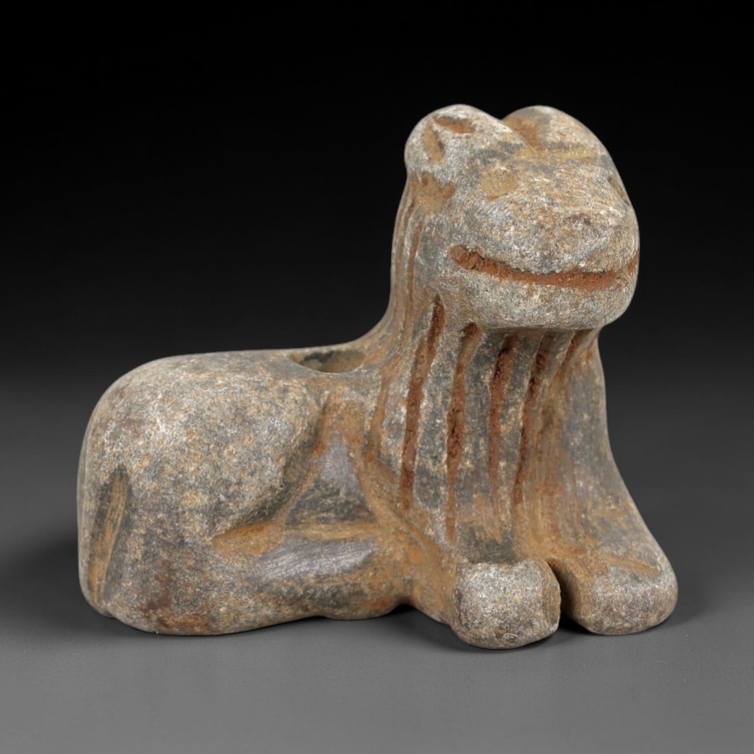 Ancient Stone Caprine Amulet - Near Eastern Animal Figurine, 41AM: This amulet is carved from speckled grey stone, depicting a stylized caprine (goat or sheep) in a recumbent, crouched posture. The piece features incised linear detailing defining the facial features,