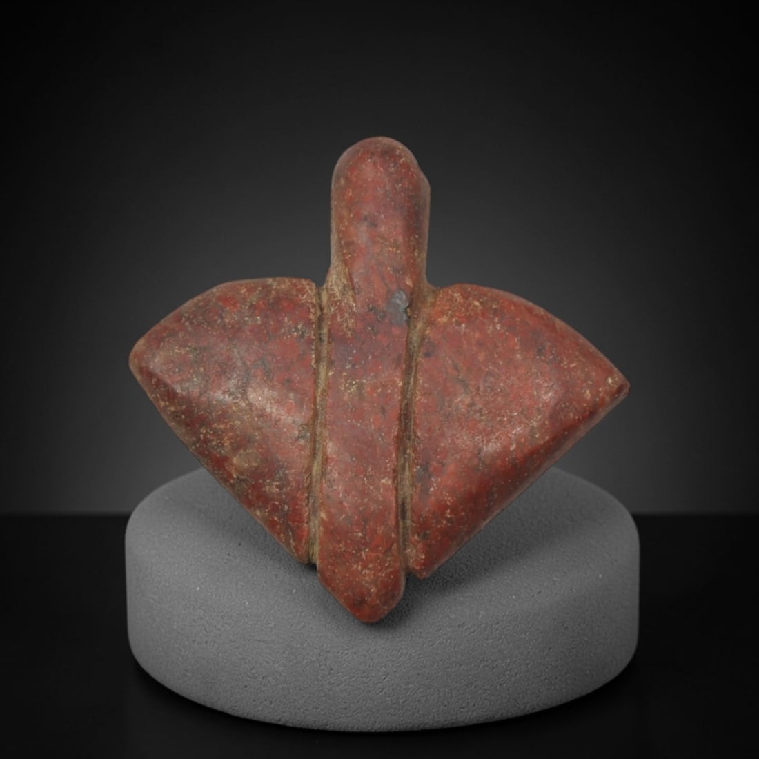 Ancient Red Stone Triangular-Form Amulet - Near Eastern Miniature Figurine, 75XP: Carved from a rich, earthy red stone with natural mineral speckling and weathered patination, this miniature amulet features a highly stylized triangular form, a distinctive geometric motif in ancient