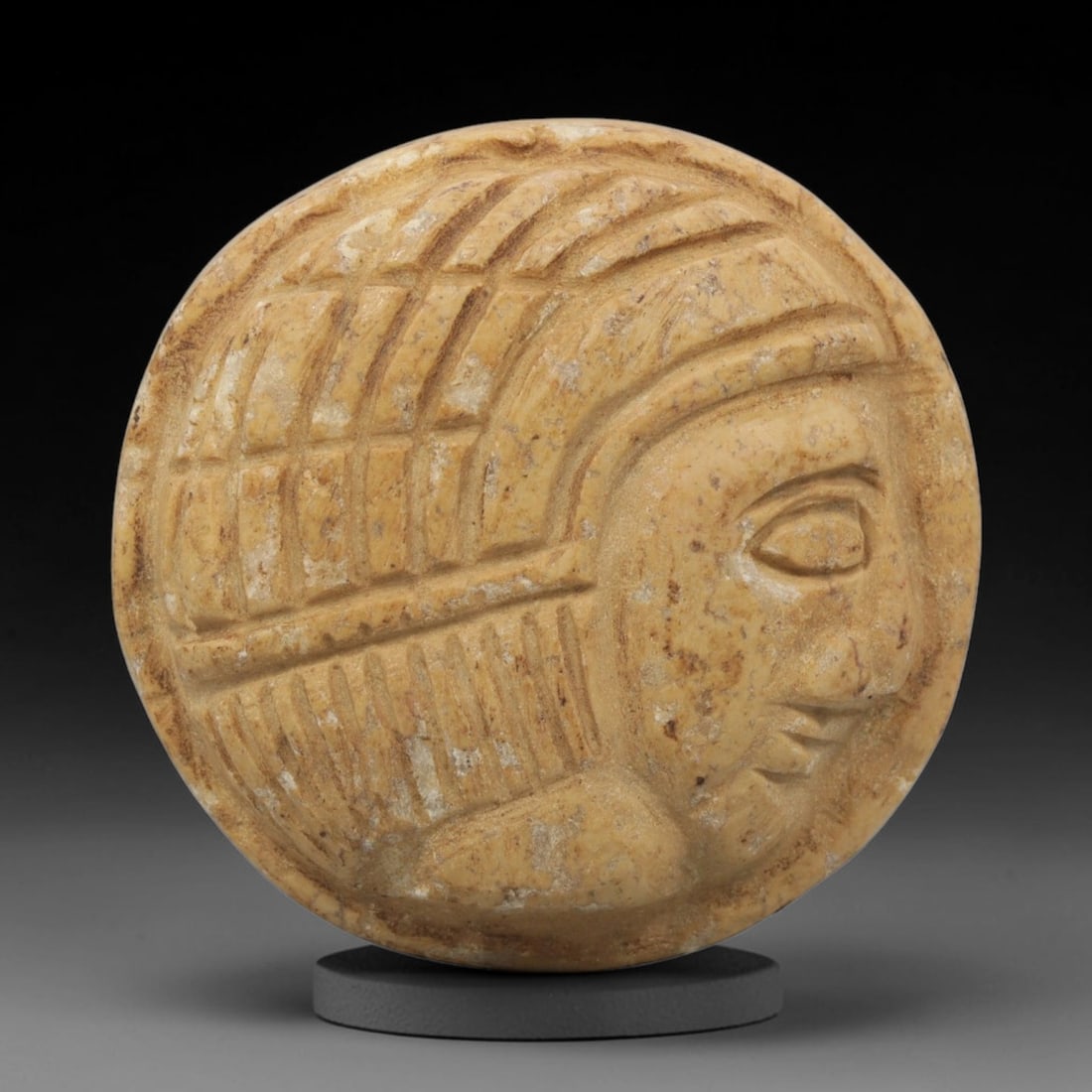 Ancient Stone Amulet - Near Eastern Bust Plaque Pendant, 13ZX: Carved from light-colored stone, the amulet is a circular plaque crafted in the ancient Near Eastern style, featuring a raised relief portrait of a human bust in profile. The surface bears incised det