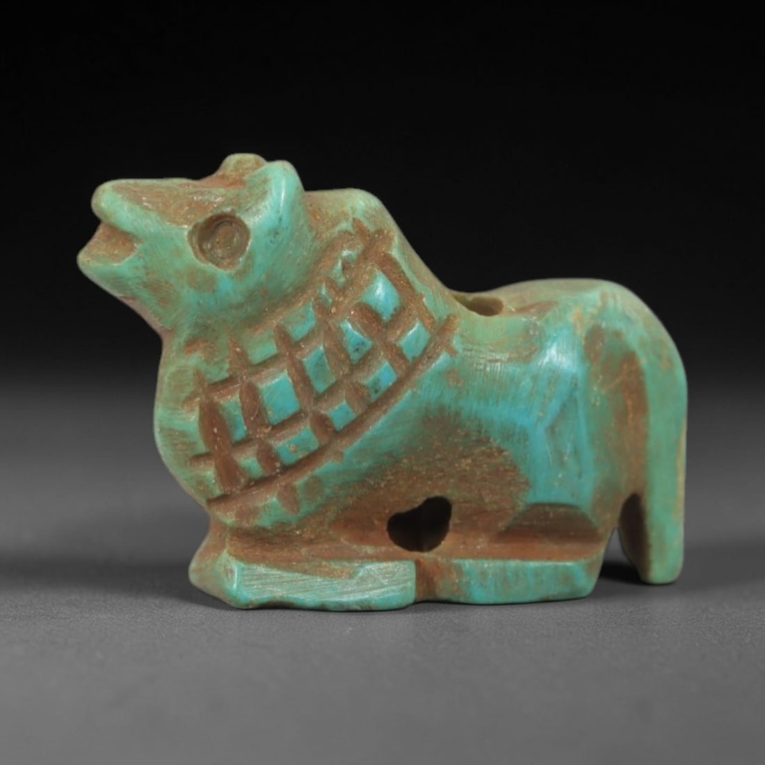 Ancient Turquoise Bovine - Near Eastern Amulet Figurine, 77AK: Carved from polished turquoise, this amulet depicts a stylized bovine figure with incised grid-patterned detailing across the torso, suspension holes for wear, and a simplified, expressive facial stru