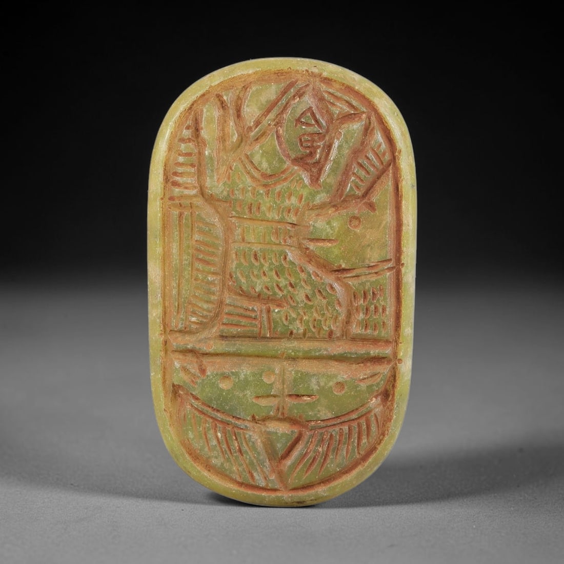 Ancient Serpentine Deity Amulet - Near Eastern Carved Pendant, 59BA: Carved from serpentine, the oval amulet features a deeply incised stylized figural composition, rendered with bold linear carving and filled with red pigment for contrast. The upper section depicts a