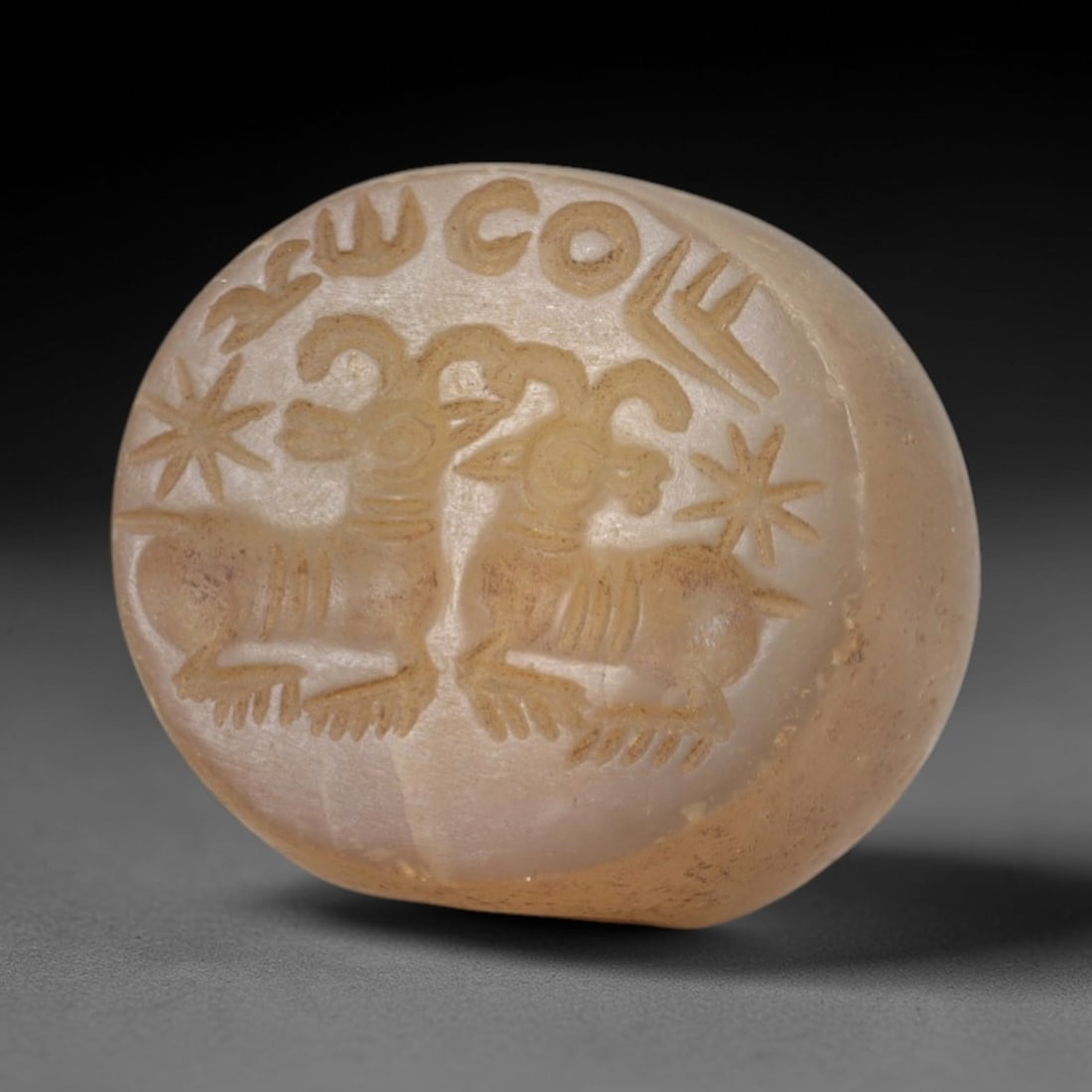 Ancient Chalcedony Stamp Seal - Sasanian Two Rams, 60AK: Carved from translucent chalcedony, this hemispherical Sasanian stamp seal features a central composition of two stylized rams with curved horns and ribbed bodies, flanked by star motifs and encircled