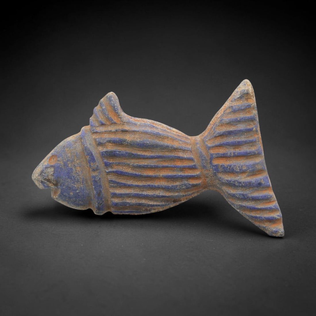 Ancient Lapis Fish Amulet - Near Eastern Carved Figurine, 7ZX: Carved from lapis lazuli, the amulet is fashioned as a three-dimensional stylized fish, with a suspension hole drilled through the dorsal fin for wear. The body is decorated with incised linear motifs