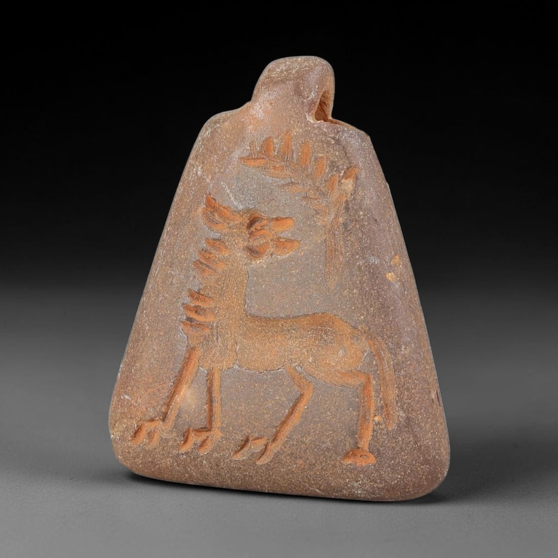 Ancient Stone Animal Amulet - Near Eastern Carved Pendant, 28BA: Carved from hardstone, the triangular amulet features a relief-carved stylized mythical or equine animal, rendered with incised detail and filled with red pigment for contrast. The animal is depicted