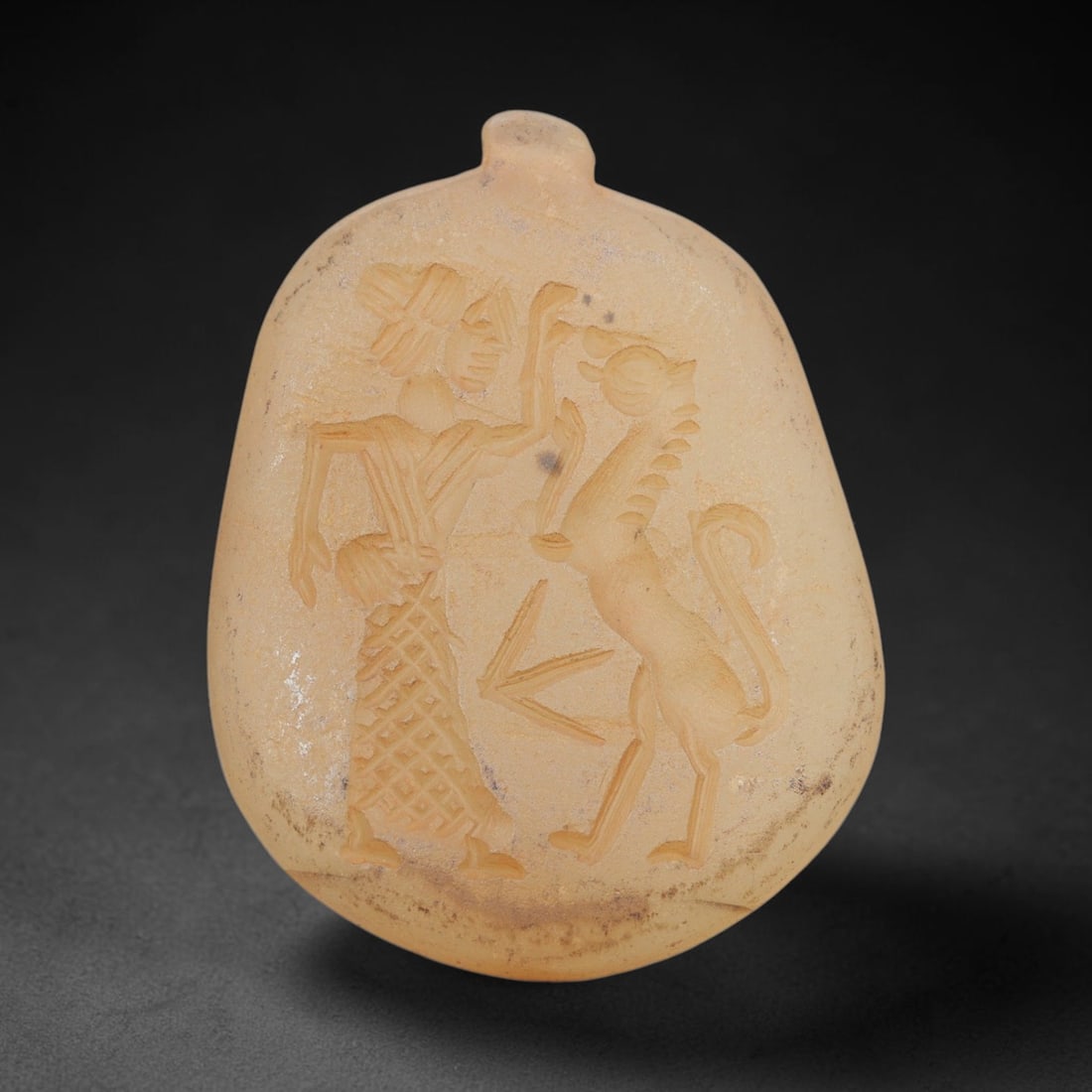 Ancient Chalcedony Amulet - Near Eastern Human & Griffin Figure, 25ZX: Carved from translucent chalcedony, this amulet features a relief scene depicting a standing human figure confronting a rampant griffin, rendered in the stylized glyptic tradition of the ancient Near