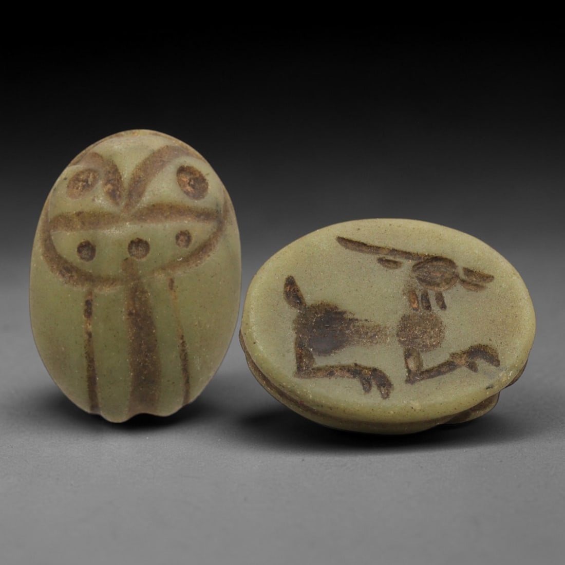 Ancient Near Eastern Scarab Stamp Seal - Gazelle Intaglio, 1ZT: Carved from a pale greenish stone, this oval scarab stamp seal features a stylized scaraboid dorsal form, with incised linear patterns defining the beetle's elytra and decorative circular motifs. The