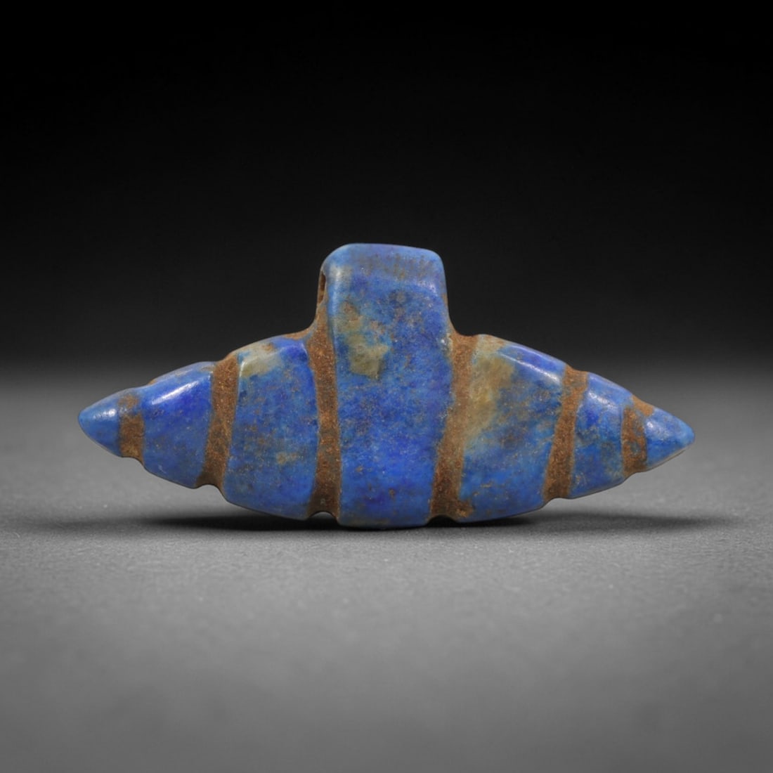 Ancient Lapis Lazuli Double Point Amulet - Egyptian Ritual Pendant, 19ZT: Carved from lapis lazuli, this amulet features a symmetrical double-pointed form with a raised central lug pierced for suspension, its body incised with horizontal bands that define its segmented stru