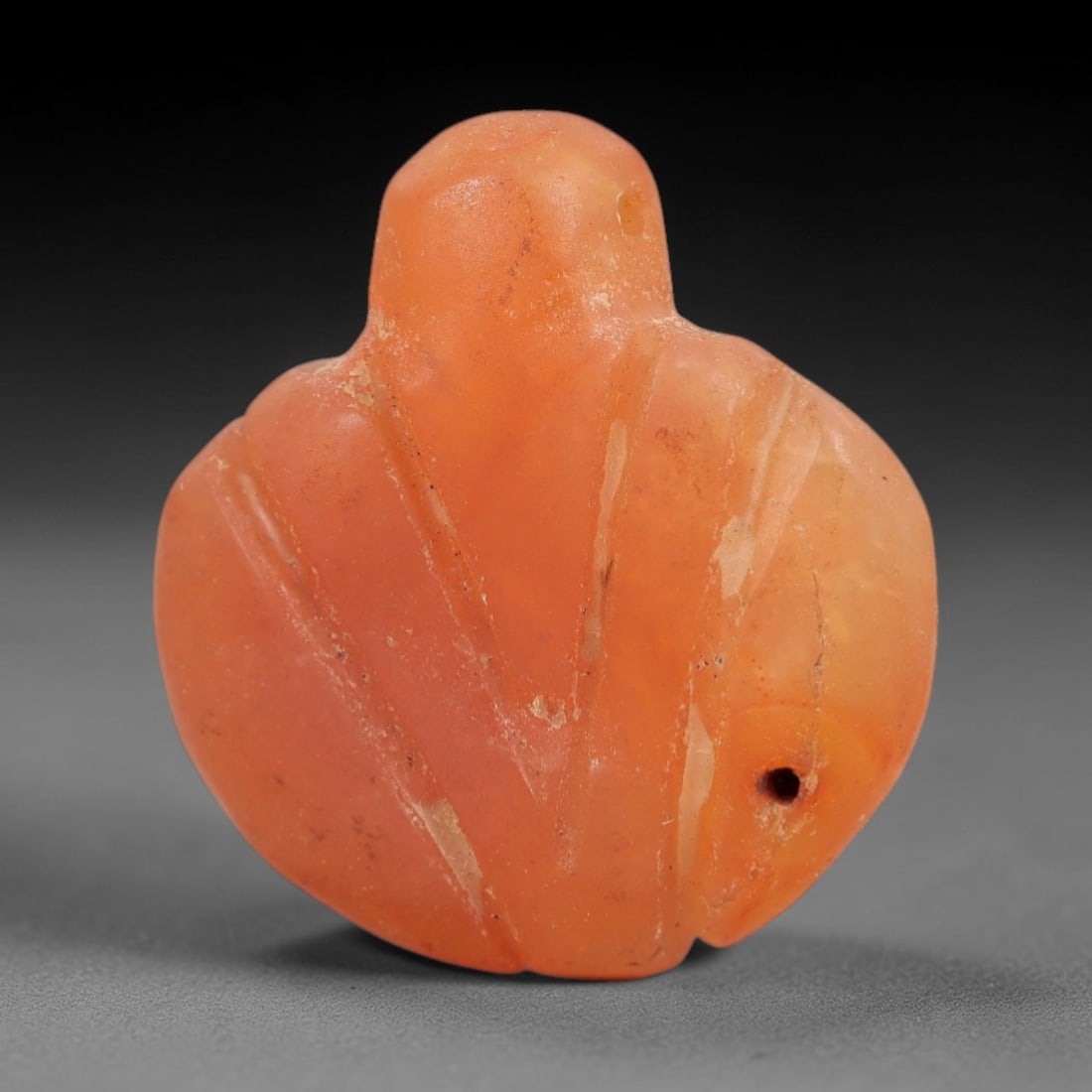 Ancient Carnelian Bird Amulet - Near Eastern Figurine, 64AJ: Carved from warm orange carnelian, this amulet is formed as a stylized bird with a rounded head and broad, curved body, featuring incised linear detailing across the surface to denote feather patterns