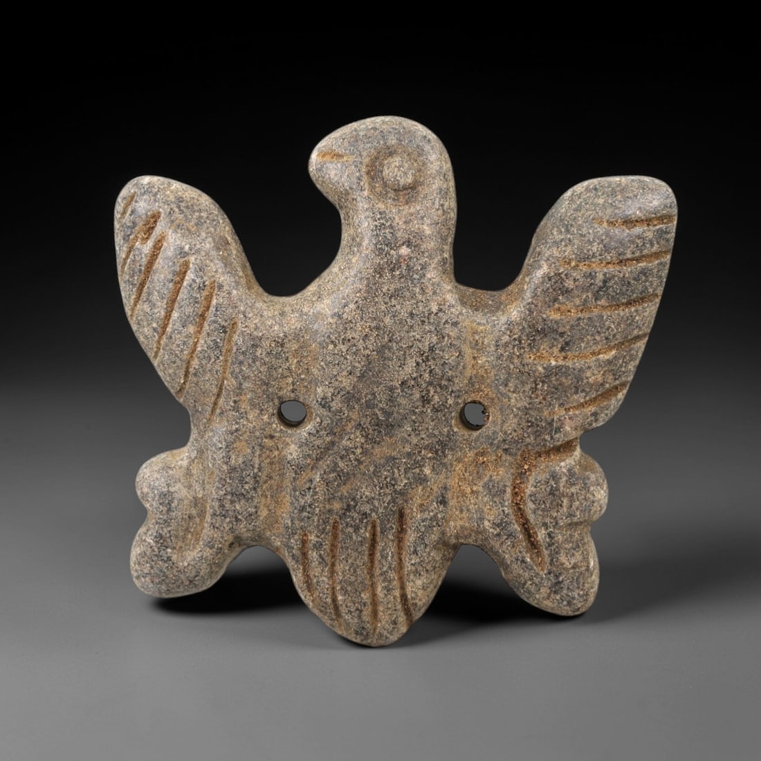 Ancient Stone Vulture Amulet - Near Eastern Bird Figure, 51AM: This amulet is carved from dark speckled stone, depicting a stylized vulture with outstretched wings and a compact body, rendered in raised relief with incised linear detailing defining the wing feath