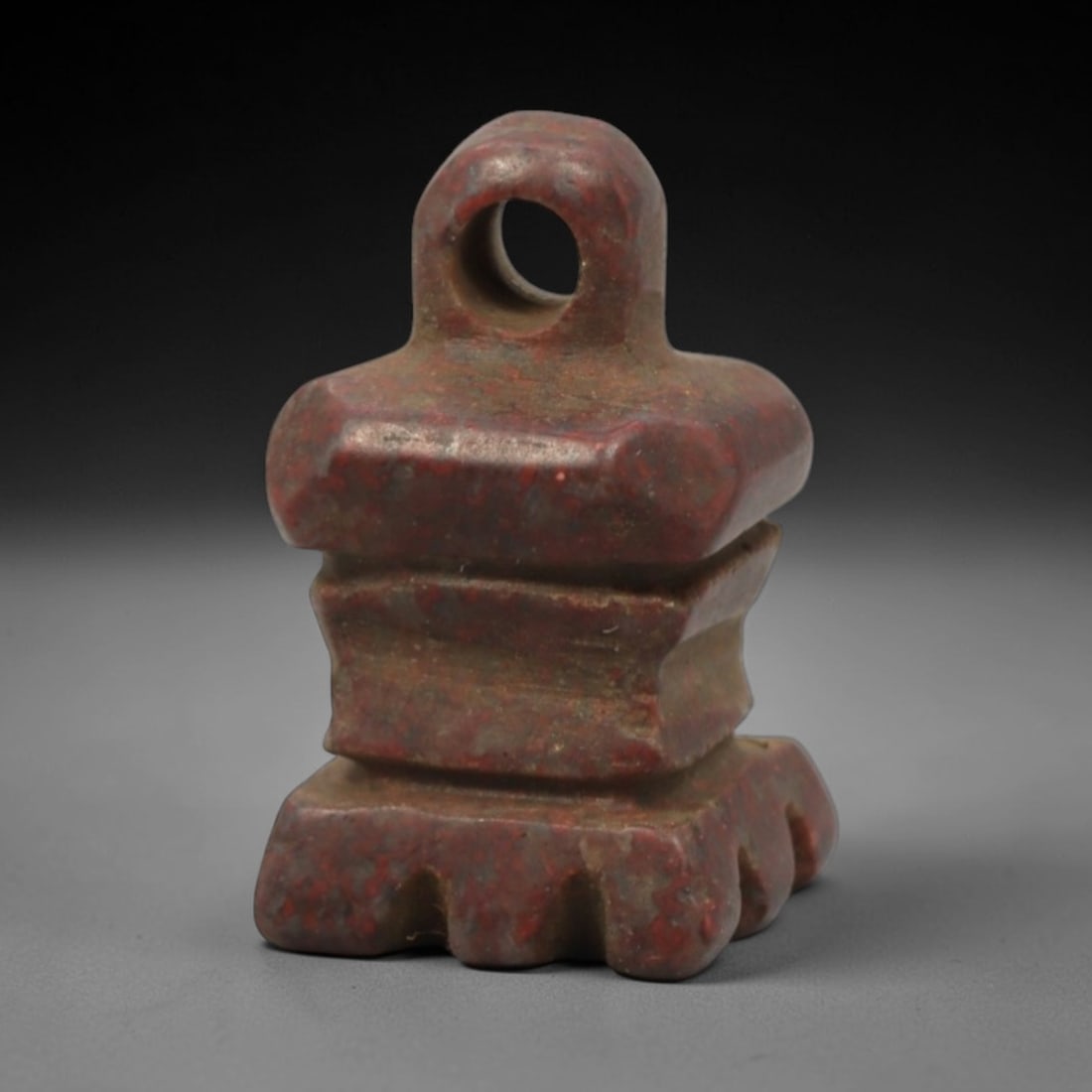 Ancient Stone Temple Amulet - Near Eastern Protective Pendant, 32XR: Carved from rich red stone with subtle mottling, this miniature amulet is shaped like a stylized temple or shrine, featuring a circular suspension loop at the top, a stepped central body, and a serrat