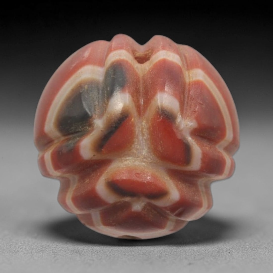 Antique Agate Floral Mask Bead - Central Asian Carved Gemstone, 3ZW: Carved from banded agate with a rich red base and creamy white-black inclusions, this bead features a stylized floral-mask hybrid motif with layered petal-like ridges and distinct facial details (eyes
