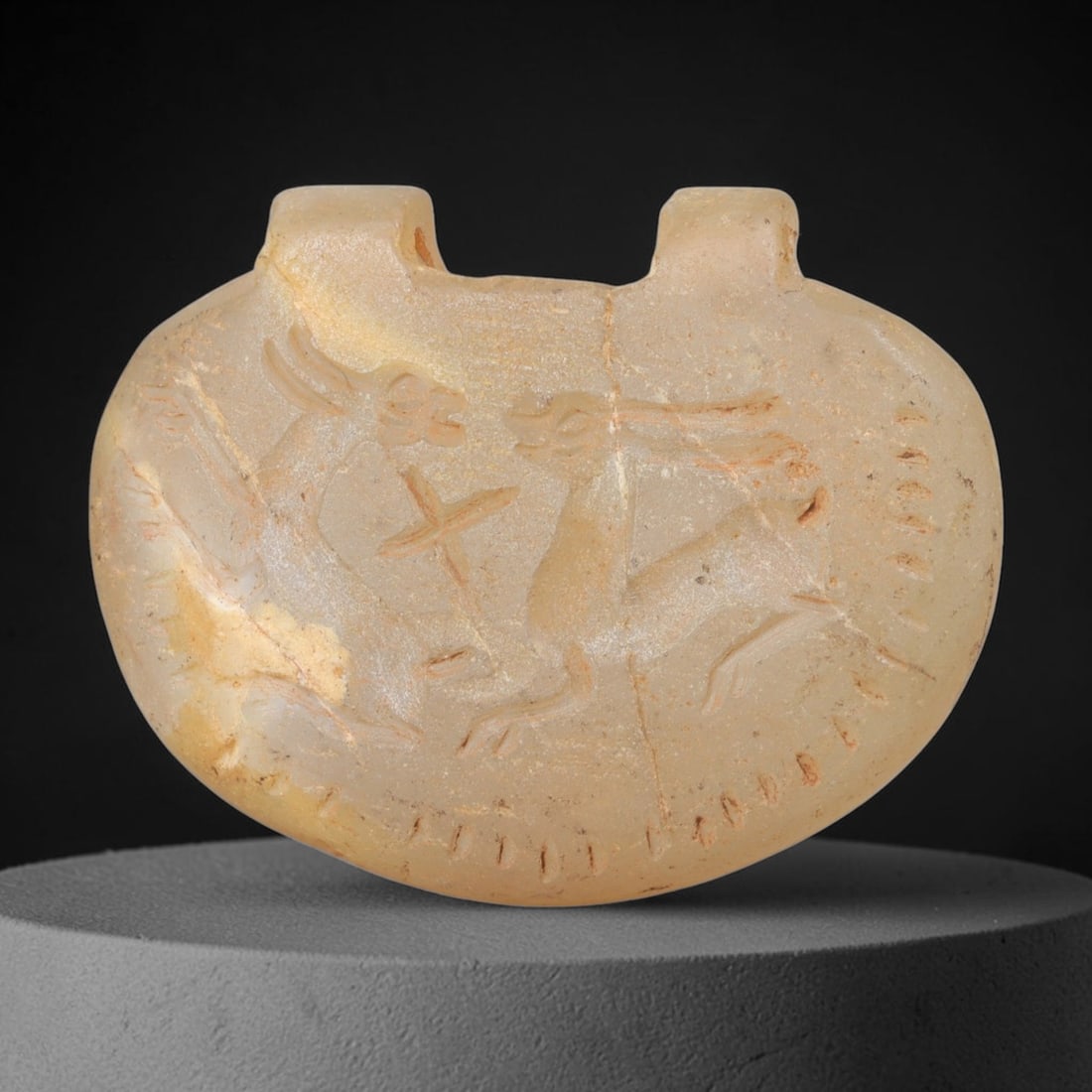 Ancient Chalcedony Animal Amulet - Near Eastern Plaque, 27FY: Carved from a pale, translucent chalcedony, this amulet takes the form of a rounded, shield-shaped plaque with two small suspension lugs at the top, characteristic of ancient Near Eastern amuletic and