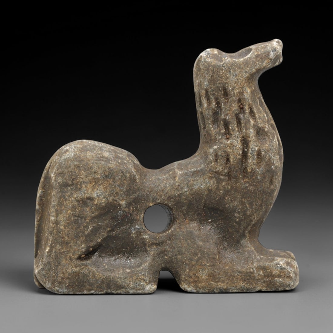 Ancient Stone Canid Amulet - Near Eastern Seated, 60ZR: Carved from dense grey-brown stone with a heavily weathered, earthy patina, executed in a stylized seated form characteristic of Near Eastern zoomorphic amulet craftsmanship. The figure depicts a cani