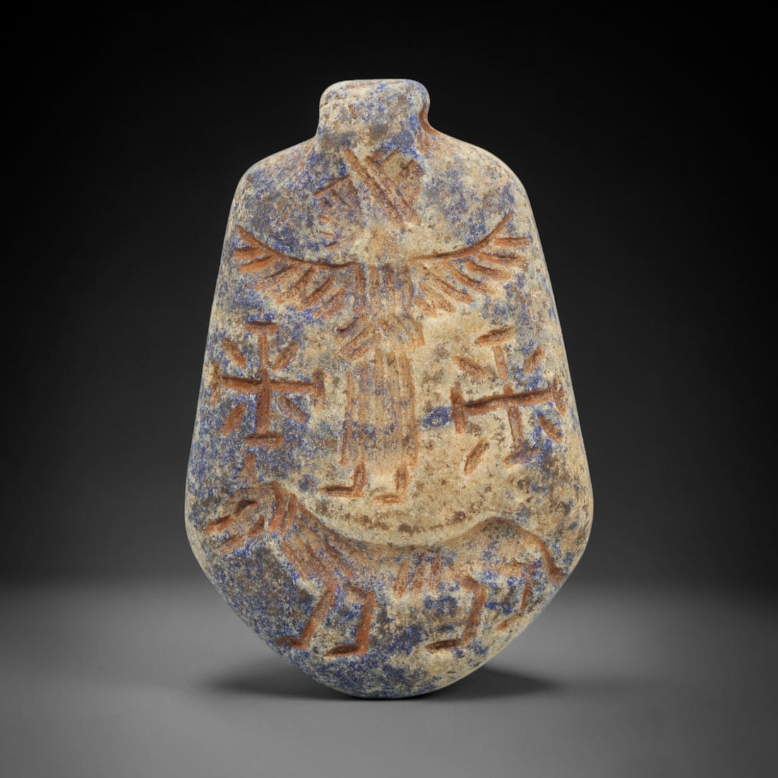 Ancient Lapis Lazuli Amulet - Near Eastern Winged Figure, 85ZT: Carved from lapis lazuli, this amulet features a relief depiction of a winged humanoid figure standing above a quadrupedal animal, rendered in the stylized glyptic tradition of the ancient Near East.