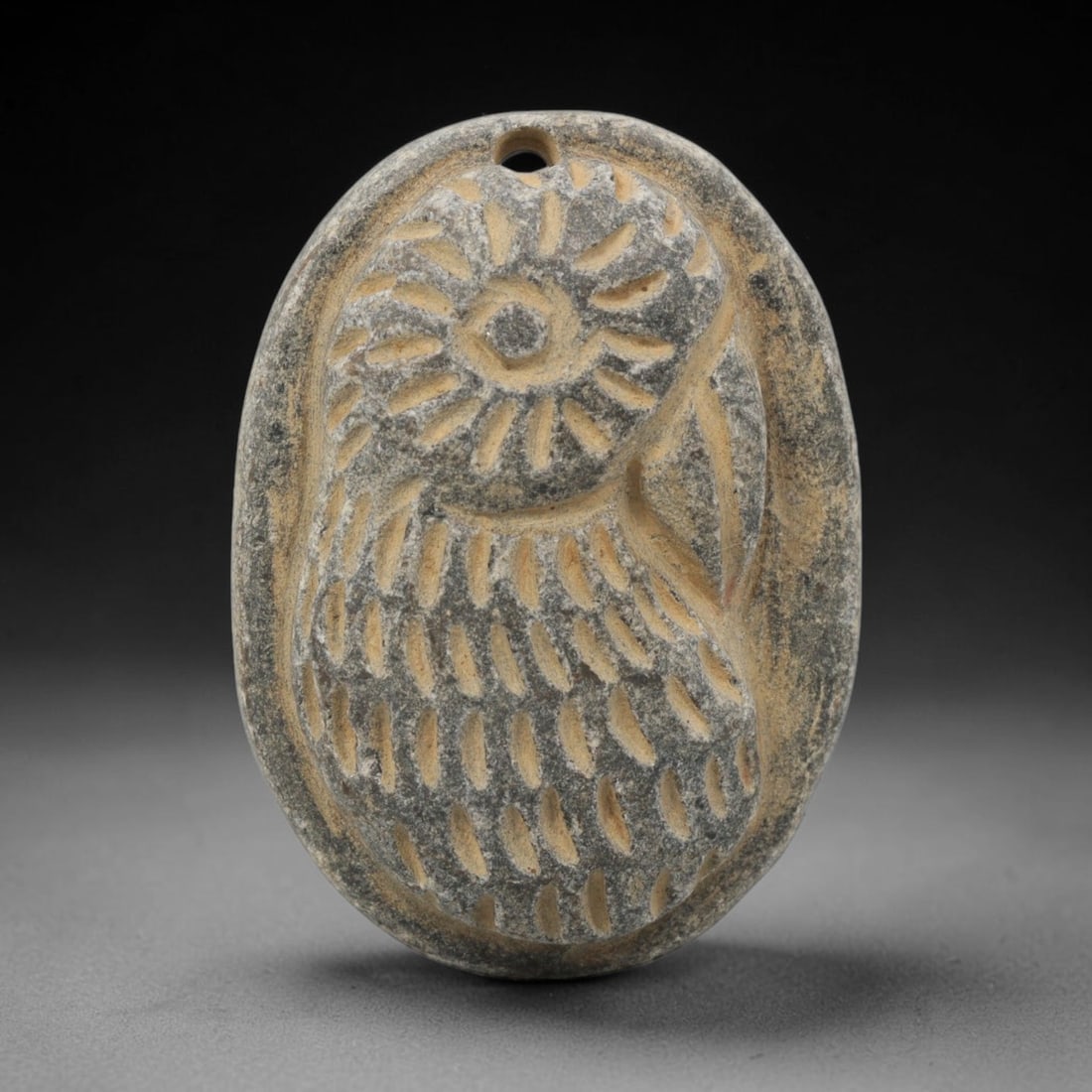Ancient Stone Amulet - Near Eastern Bird Head Pendant, 41ZX: Carved from stone, the amulet is an oval plaque with a drilled suspension hole at the top, crafted in the ancient Near Eastern style. The front surface bears a raised relief bird head motif, with inci