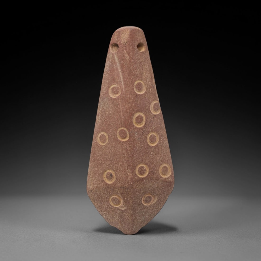 Ancient Stone Amulet - Near Eastern Geometric Pendant, 1XR: This amulet is carved from a fine-grained, reddish-brown stone, shaped into an elongated teardrop form with two perforated suspension holes at the upper edge, confirming its use as a wearable protecti
