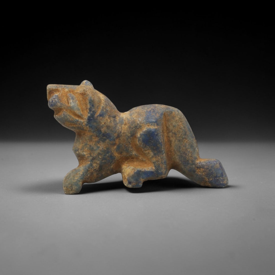 Ancient Lapis Lazuli Feline - Near Eastern Amulet Figurine, 13XT: Carved from lapis lazuli, this amulet depicts a crouched feline in a dynamic predatory stance. The head is raised with incised eye and mouth detailing, while the body is compact and muscular, with a v