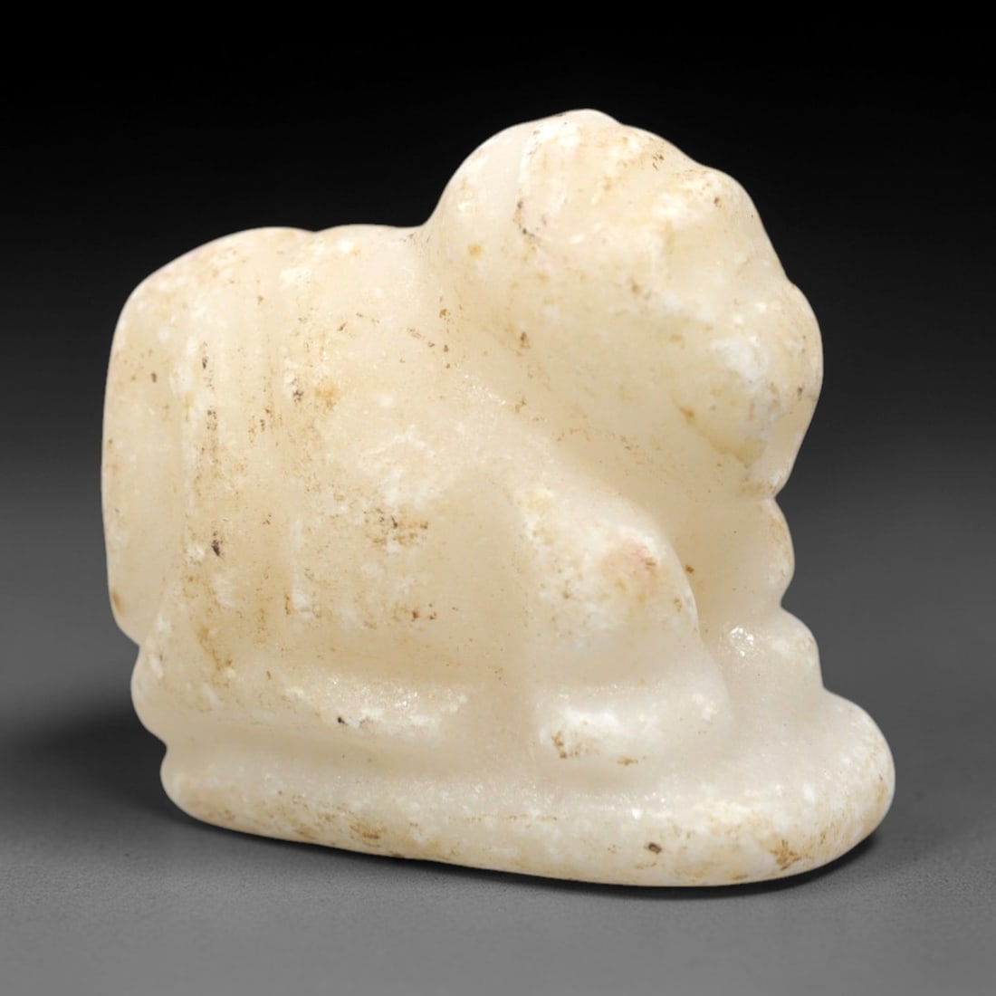 Ancient Calcite Feline - Egyptian Amulet Figurine, 60XV: Carved from translucent white calcite, this compact feline amulet is rendered in a stylized recumbent pose, with simplified facial and bodily forms consistent with ancient Egyptian amuletic craftsmans