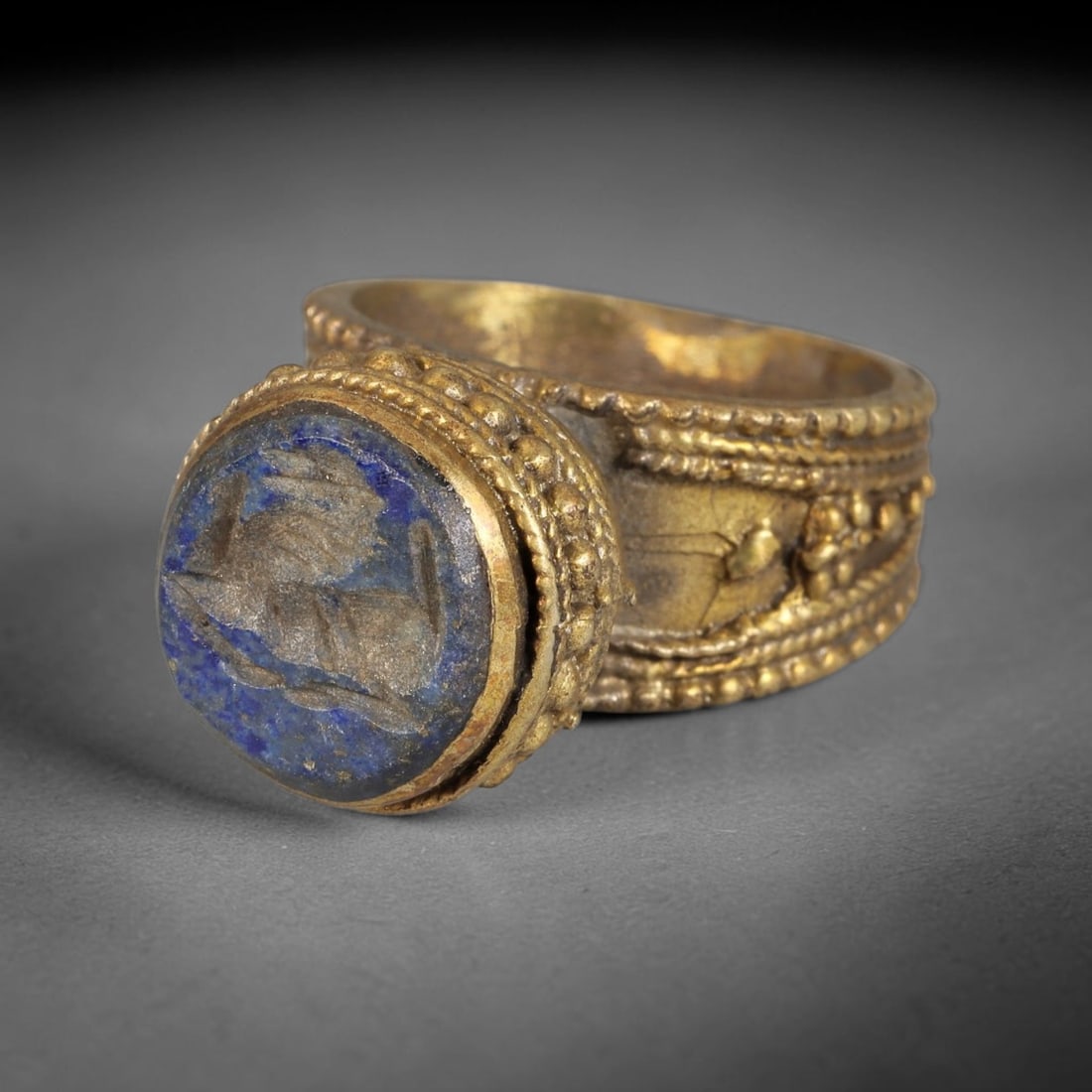 Antique Qajar Dynasty Lapis Lazuli Intaglio Brass Ring - Size 9 US, 60BA: Crafted from brass, this ring features a circular lapis lazuli intaglio panel carved with a stylized quadruped, executed in the traditional Qajar style. The brass band displays ornate, layered granula