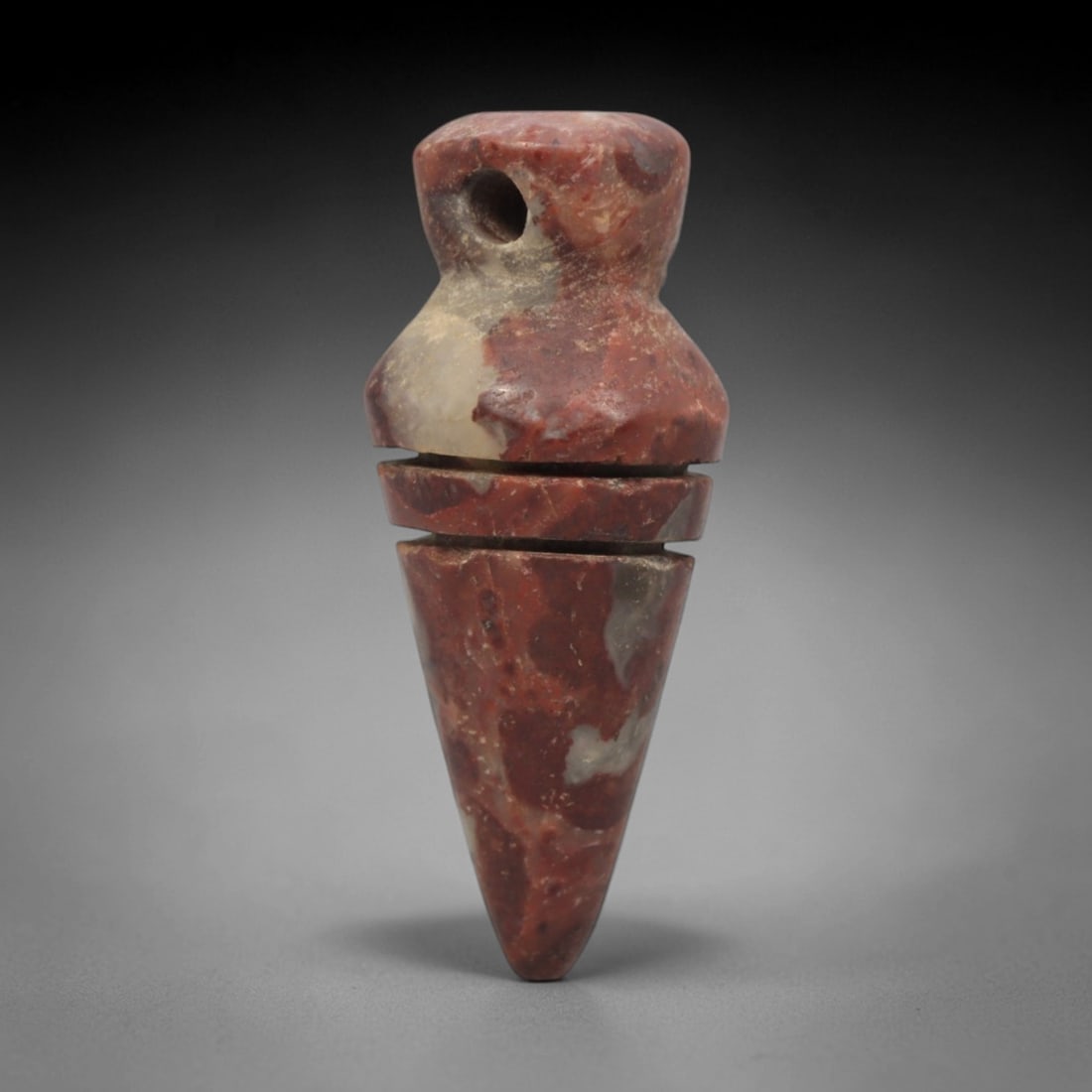 Ancient Near Eastern Red Stone Conical Amulet - Carved Pendant Figure, 32ZV: This amulet is carved from a striking variegated red-and-white stone, likely brecciated jasper, featuring a segmented conical form. The piece consists of a rounded suspension loop with a drilled hole,