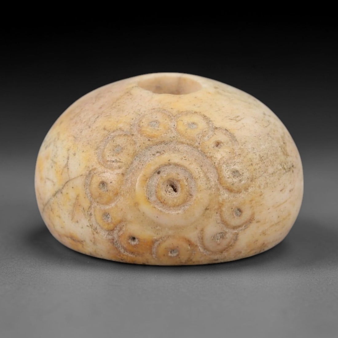 Ancient Near Eastern Bone Spindle Whorl - Dot-in-Circle Motif, 87AH: Carved from ancient bone, this Near Eastern spindle whorl features a continuous dot-in-circle motif encircling its central perforation, a design with apotropaic significance in ancient Near Eastern cu
