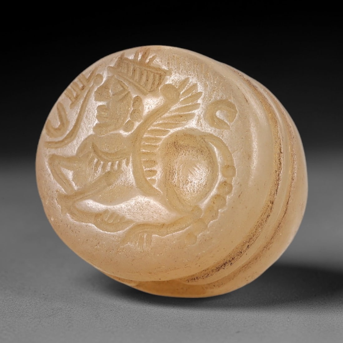 Ancient Chalcedony Stamp Seal - Near Eastern Winged Creature, 12AL: This hemispherical stamp seal is carved from translucent chalcedony, its flat face depicting a winged hybrid creature with a humanoid upper body, feathered wings, and a quadrupedal lower body, alongsi