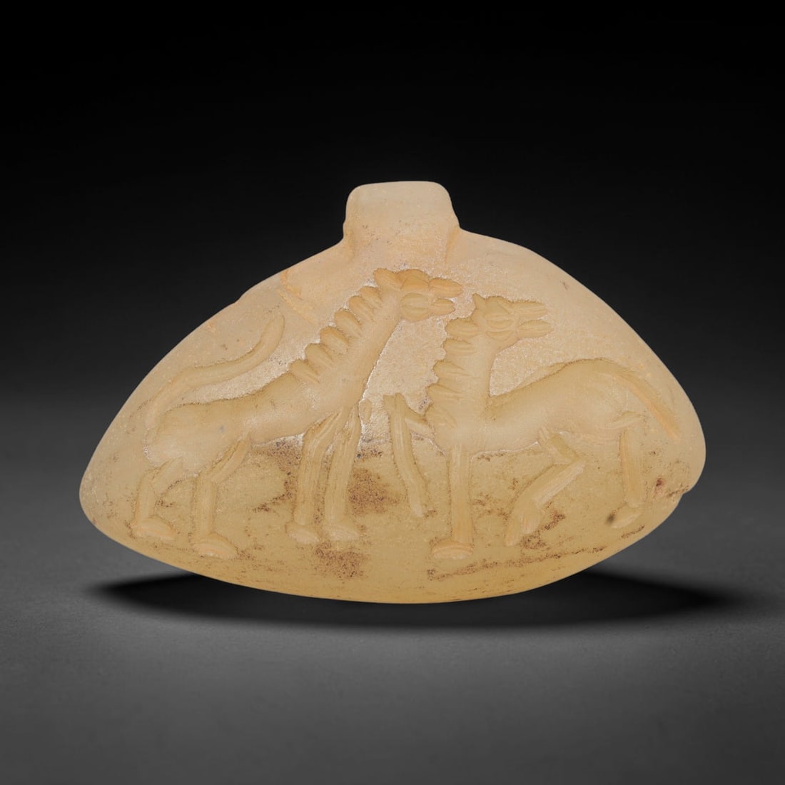 Ancient Chalcedony Amulet - Near Eastern Animal Figure, 15ZX: Crafted from translucent chalcedony, this amulet features a finely carved relief depicting two confronting animal figures, likely canids or equids, rendered in a stylized Near Eastern iconographic tra