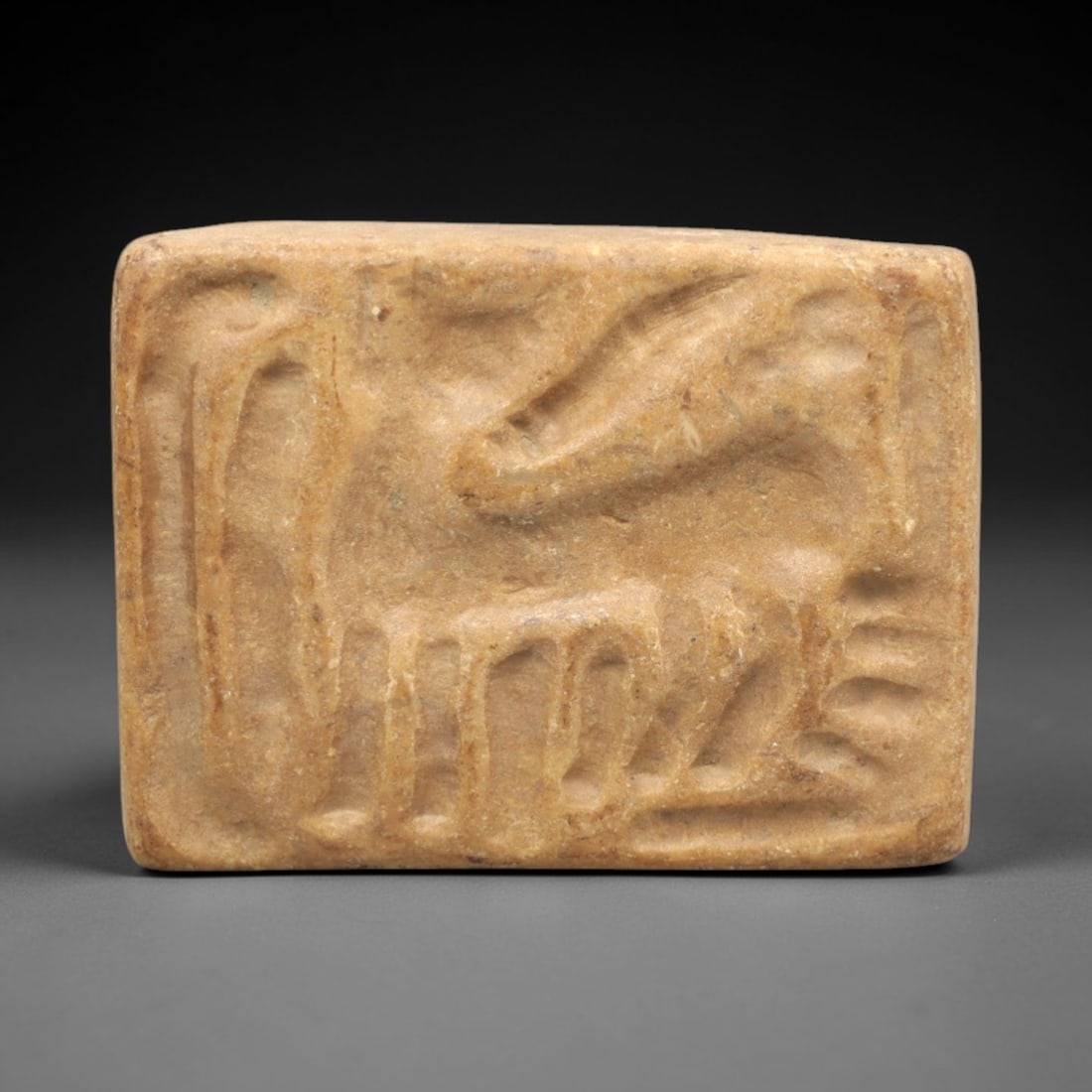 Ancient Steatite Stamp Seal - Near Eastern Stag Amulet, 96ZP: Carved from light tan steatite, this rectangular stamp seal displays a stylized stag motif in raised relief, accompanied by linear decorative elements, characteristic of Near Eastern glyptic tradition