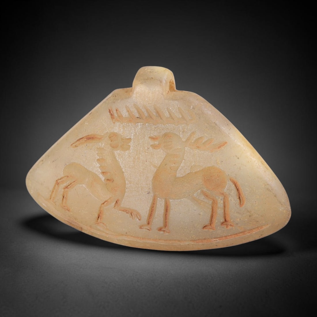 Ancient Chalcedony Animal Amulet - Near Eastern Plaque, 33FY: Carved from a pale, translucent chalcedony, this amulet takes the form of a triangular plaque with a small suspension lug at the top, characteristic of ancient Near Eastern amuletic and glyptic tradit