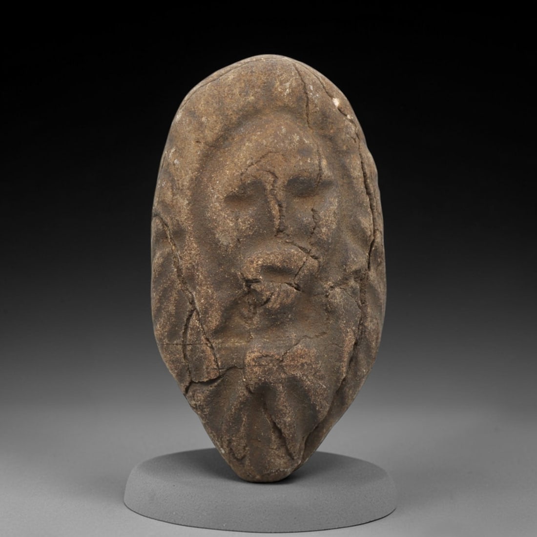 Ancient Stone Figural Amulet - Near Eastern Christian Head, 73ZV: Carved from an elongated stone, this piece features a high-relief depiction of a bearded male head, likely representing a Christian saint or holy figure, with incised lines defining the facial feature