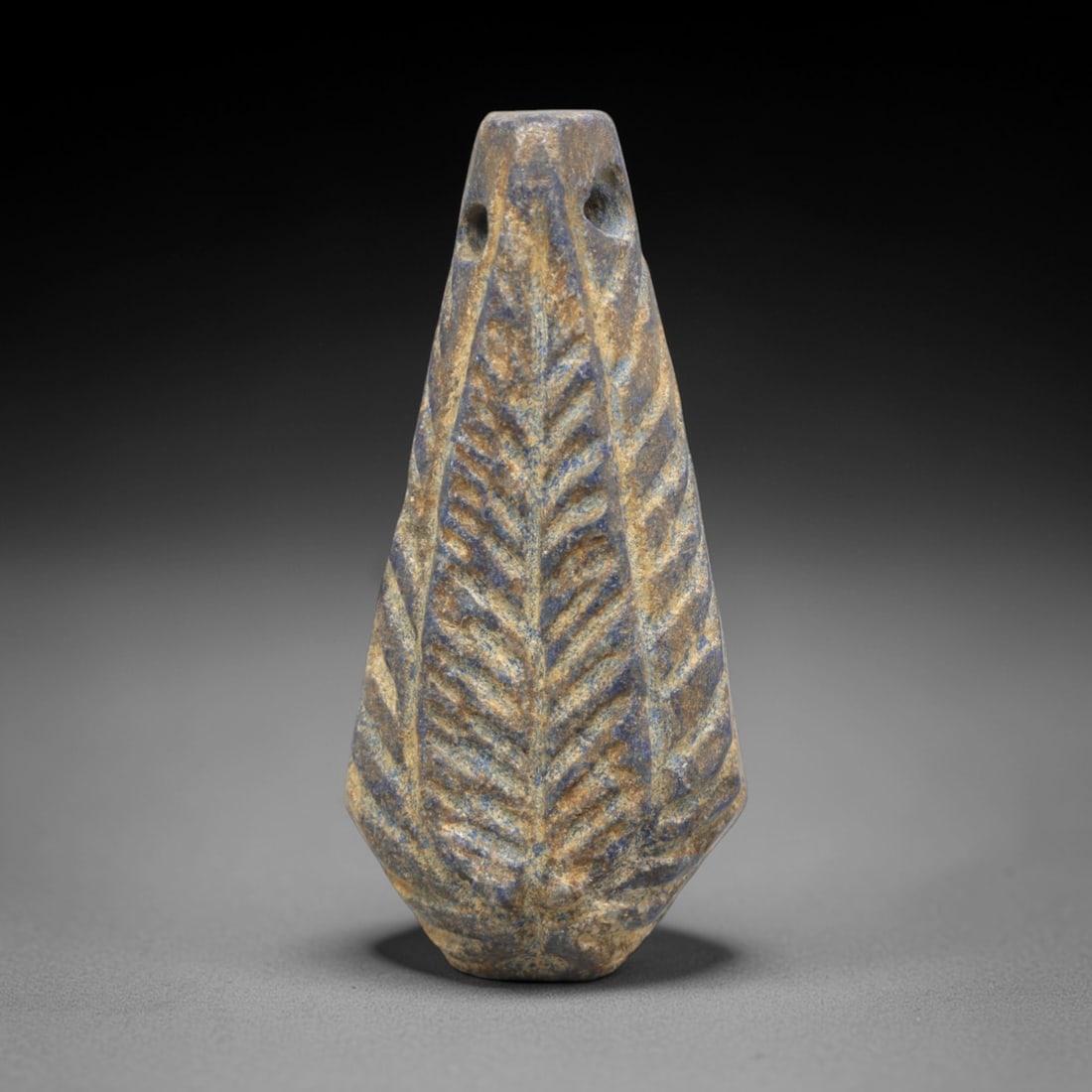 Ancient Lapis Lazuli Amulet - Near Eastern Leaf Motif, 62ZP: This amulet is carved from lapis lazuli, shaped into a teardrop form with two suspension holes at the upper edge, confirming its function as a wearable talisman. The surface is decorated with deeply i