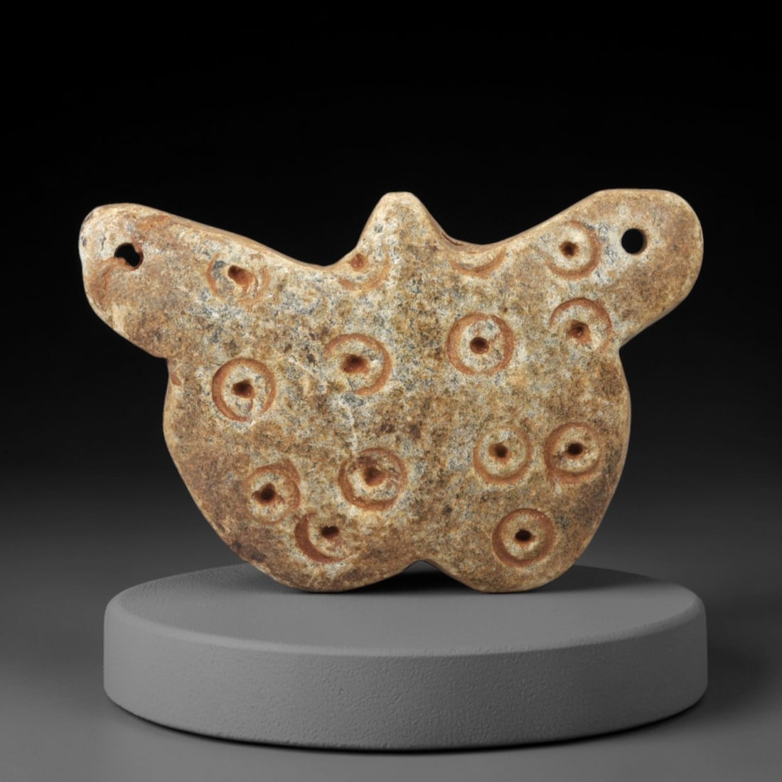 Ancient Steatite Amulet - Near Eastern Circular Motif Figurine, 98AK: Carved from steatite, this amulet features a stylized, winged or shield-like form with multiple incised circular motifs, each containing a central dot, and two lateral suspension holes for wearable us