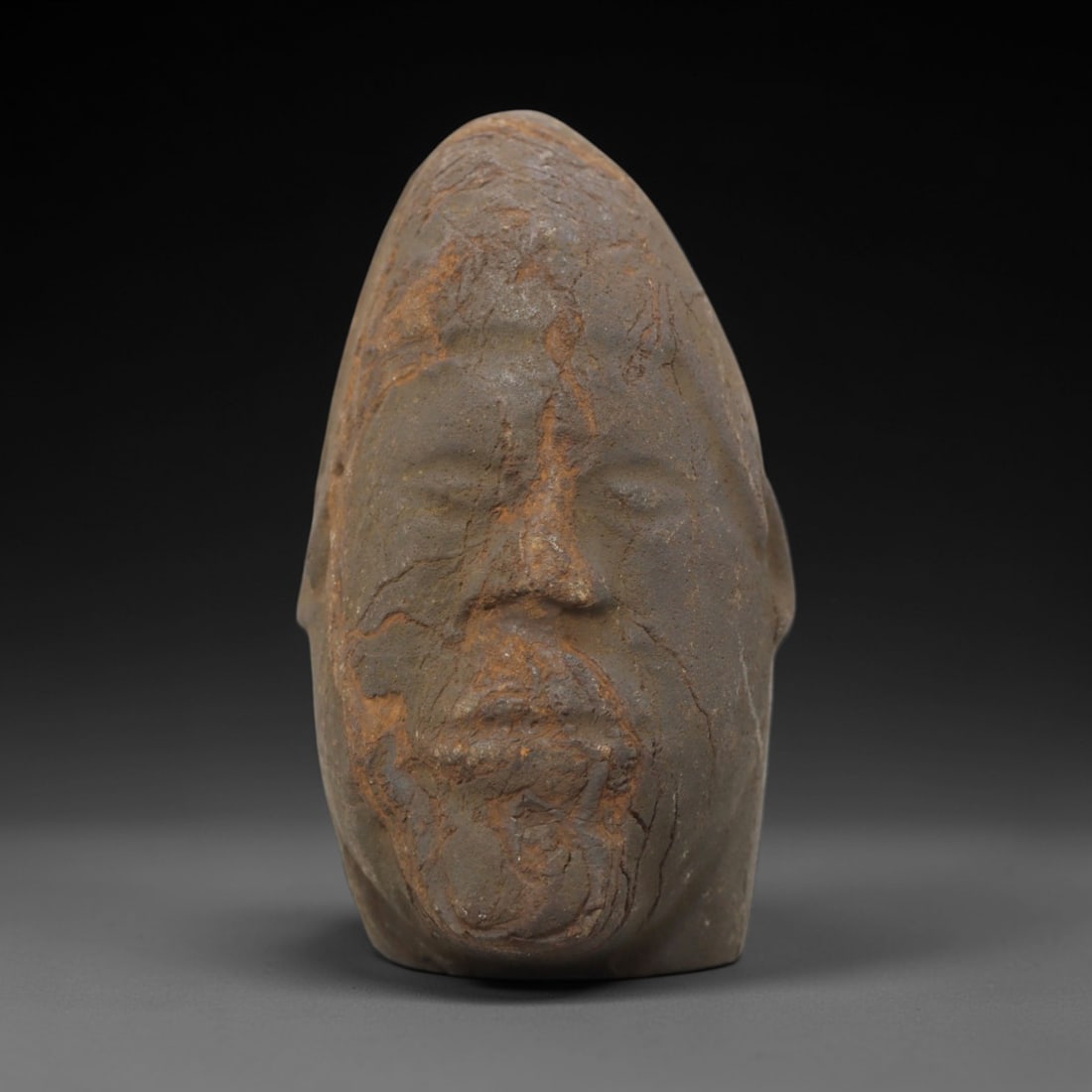 Ancient Stone Bust - African Anthropomorphic Figurine, 83FW: Carved from a coarse, weathered stone, this African bust presents a stylized human head with a tapered, conical upper form, recessed eye sockets, a defined nasal ridge, and a stylized beard or facial