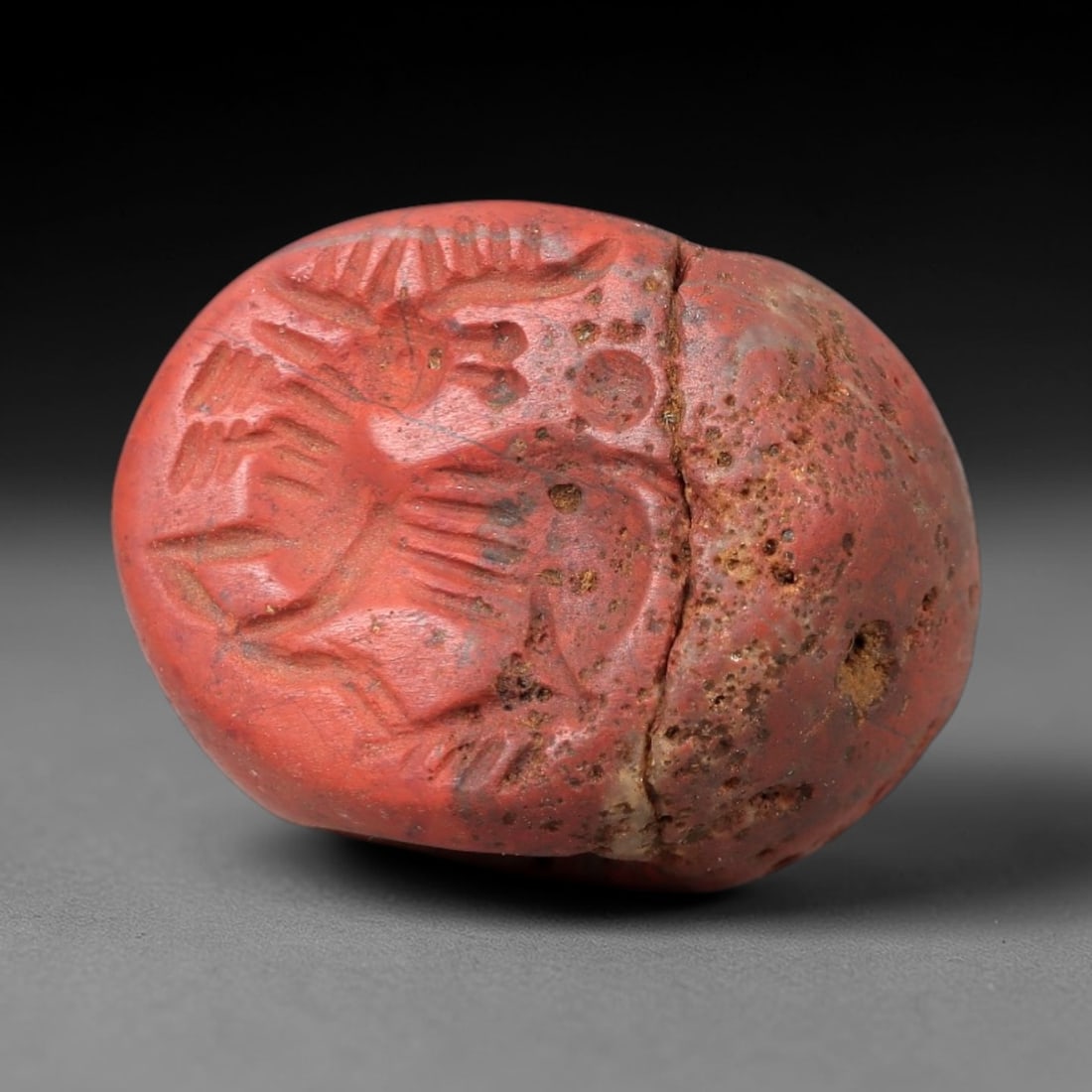 Ancient Jasper Stamp Seal - Near Eastern Stag Figure, 95AM: Carved from porous red jasper, this hemispherical stamp seal depicts a stylized stag with prominent branching antlers, linear incised details defining its body and limbs, and a circular element adjace