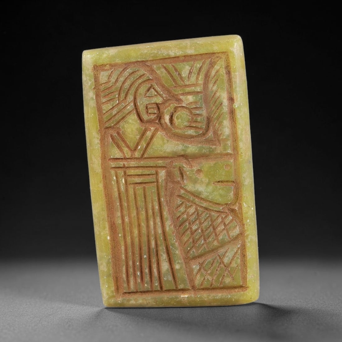 Ancient Serpentine Amulet - Near Eastern Carved Pendant, 58BA: Carved from serpentine, the rectangular amulet features a deeply incised stylized figural composition, rendered with bold linear carving and filled with red pigment for contrast. The design depicts a
