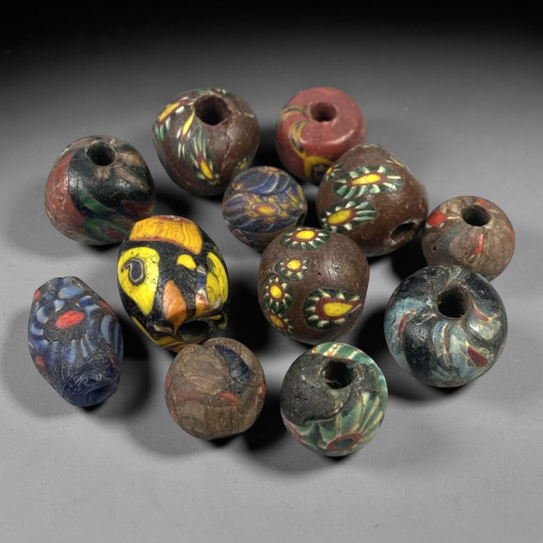 Antique Venetian Glass Beads - 12 Pieces, 55FX: This set of 12 antique Venetian glass beads features hand-formed spherical and slightly irregular shapes, crafted from polychrome glass with intricate mosaic and cane-work patterns characteristic of t