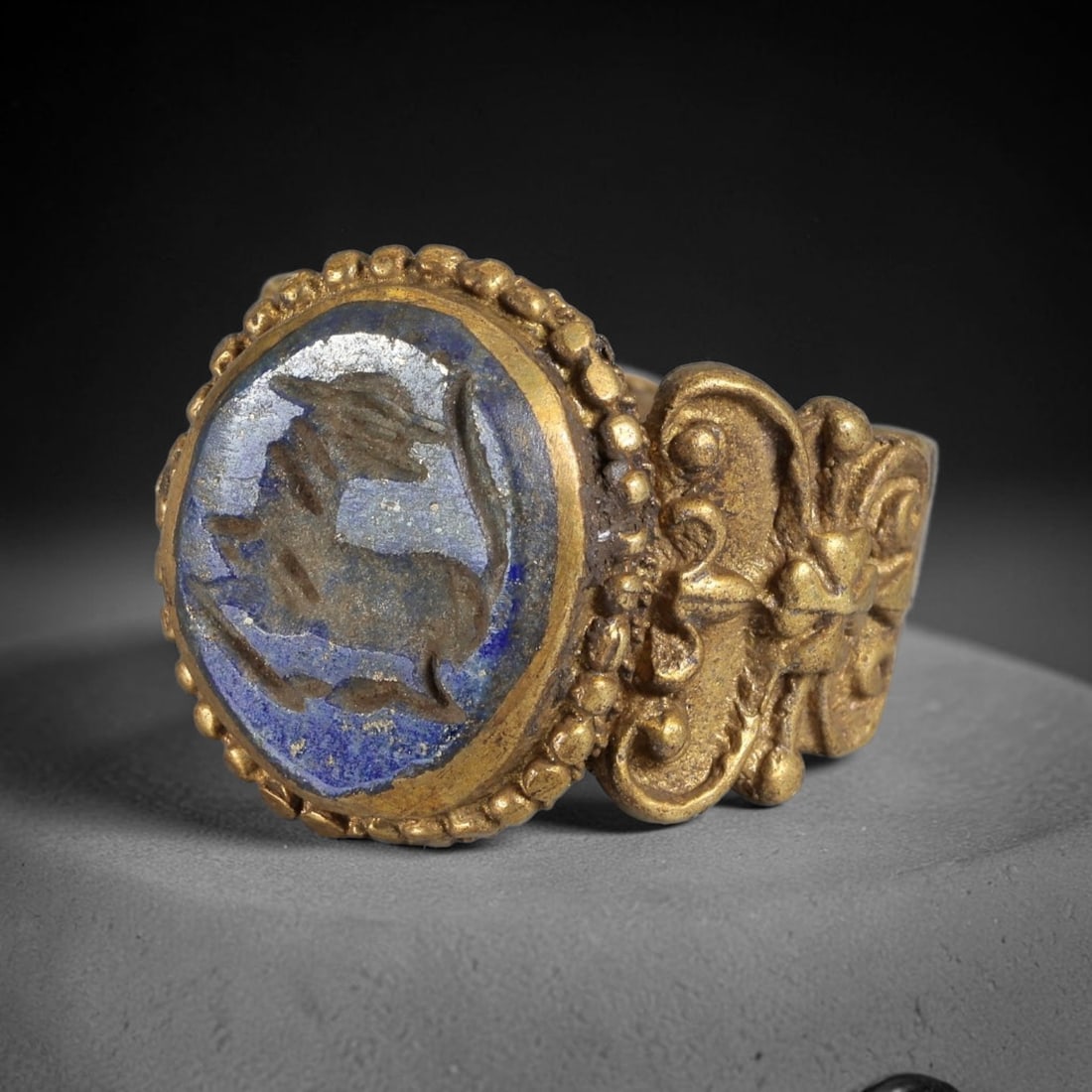 Antique Qajar Dynasty Lapis Lazuli Intaglio Brass Ring - Size 10 US, 71BA: Crafted from brass, this ring features an oval lapis lazuli intaglio panel carved with a stylized quadruped, executed in the traditional Qajar style. The brass band displays ornate, relief-carved meta
