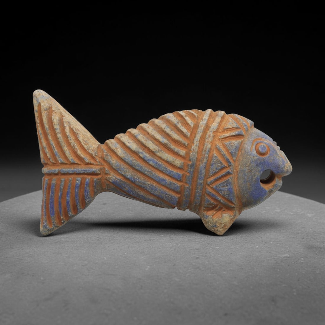 Ancient Lapis Fish Amulet - Near Eastern Carved Figurine, 86ZT: Carved from lapis lazuli, the amulet is fashioned as a three-dimensional stylized fish, with a suspension hole drilled through the dorsal fin for wear. The body is decorated with incised linear motifs