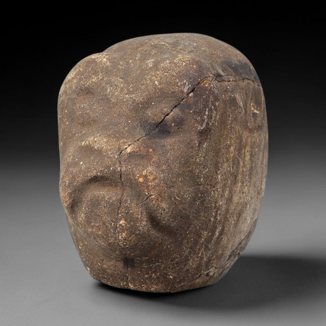 Ancient Stone Zoomorphic Maskette - Near Eastern Amulet, 39WJ: Carved from a dense, coarse stone, this artifact takes the form of a stylized zoomorphic face maskette, rendered with simplified, archaic features. The form is characterized by a broad, rounded snout,