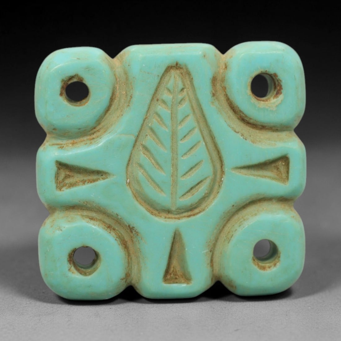 Antique Turquoise Bead Amulet - Central Asian, 53ZW: Carved from vibrant turquoise, this square bead amulet features a central incised leaf motif, flanked by geometric triangular details and four corner suspension holes for wearable use. The piece exhib