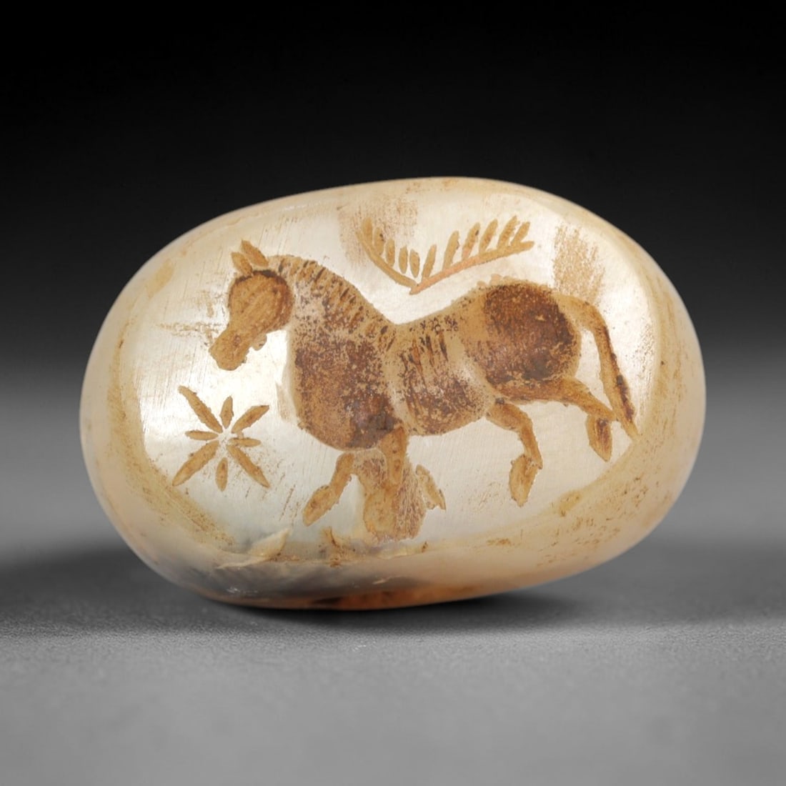 Ancient Chalcedony Stamp Seal - Near Eastern Horse Figure, 42ZS: Crafted from translucent chalcedony, this oval stamp seal bears an incised scene of a galloping horse, accompanied by a stylized star and plant motif, rendered with linear detailing to define the anim