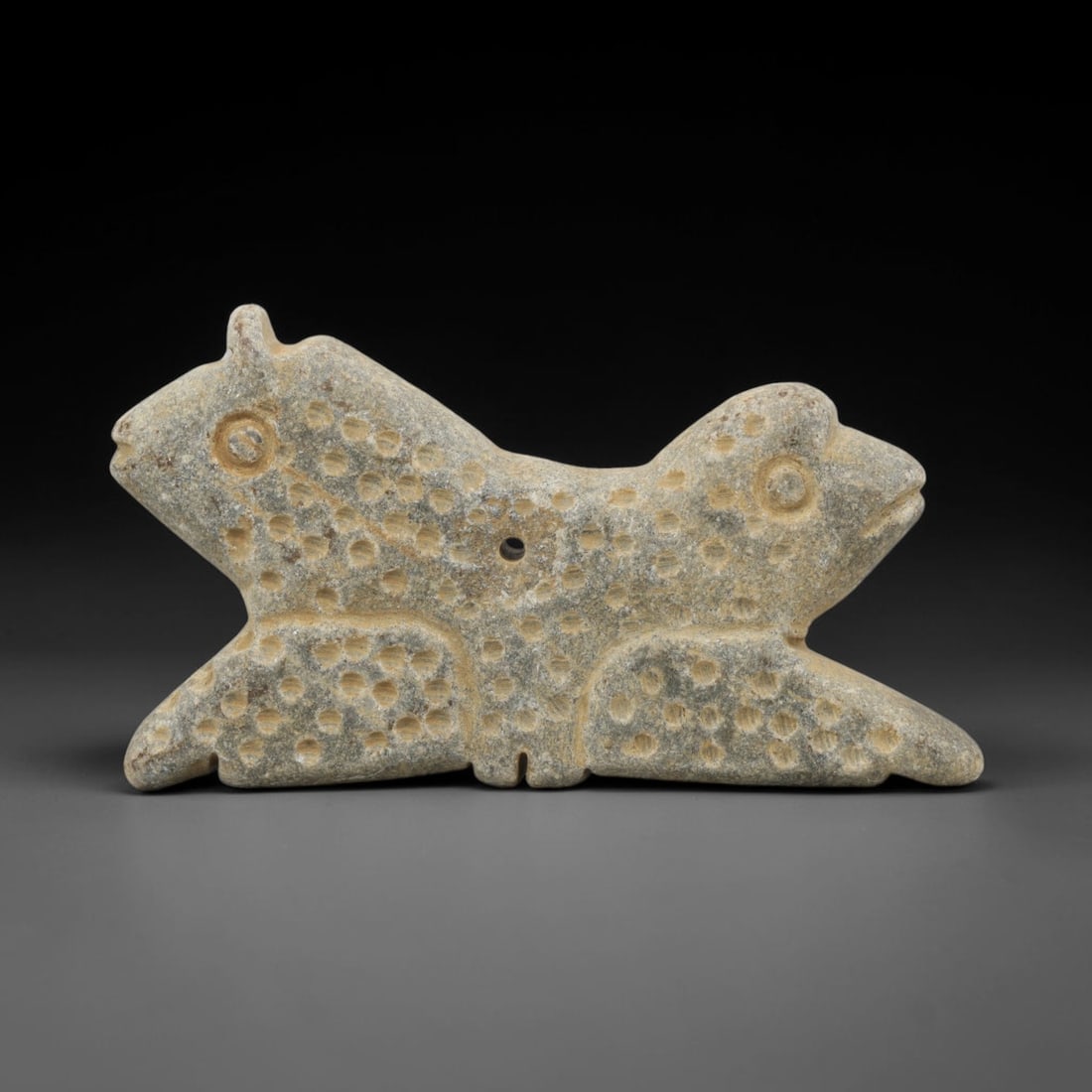 Ancient Near Eastern Schist Double Zoomorphic Head Amulet, 32ZX: This ancient amulet is carved from schist, a metamorphic stone, in the form of a double-headed zoomorphic figure, likely representing two stylized felines or mythical beasts joined at a shared body. T