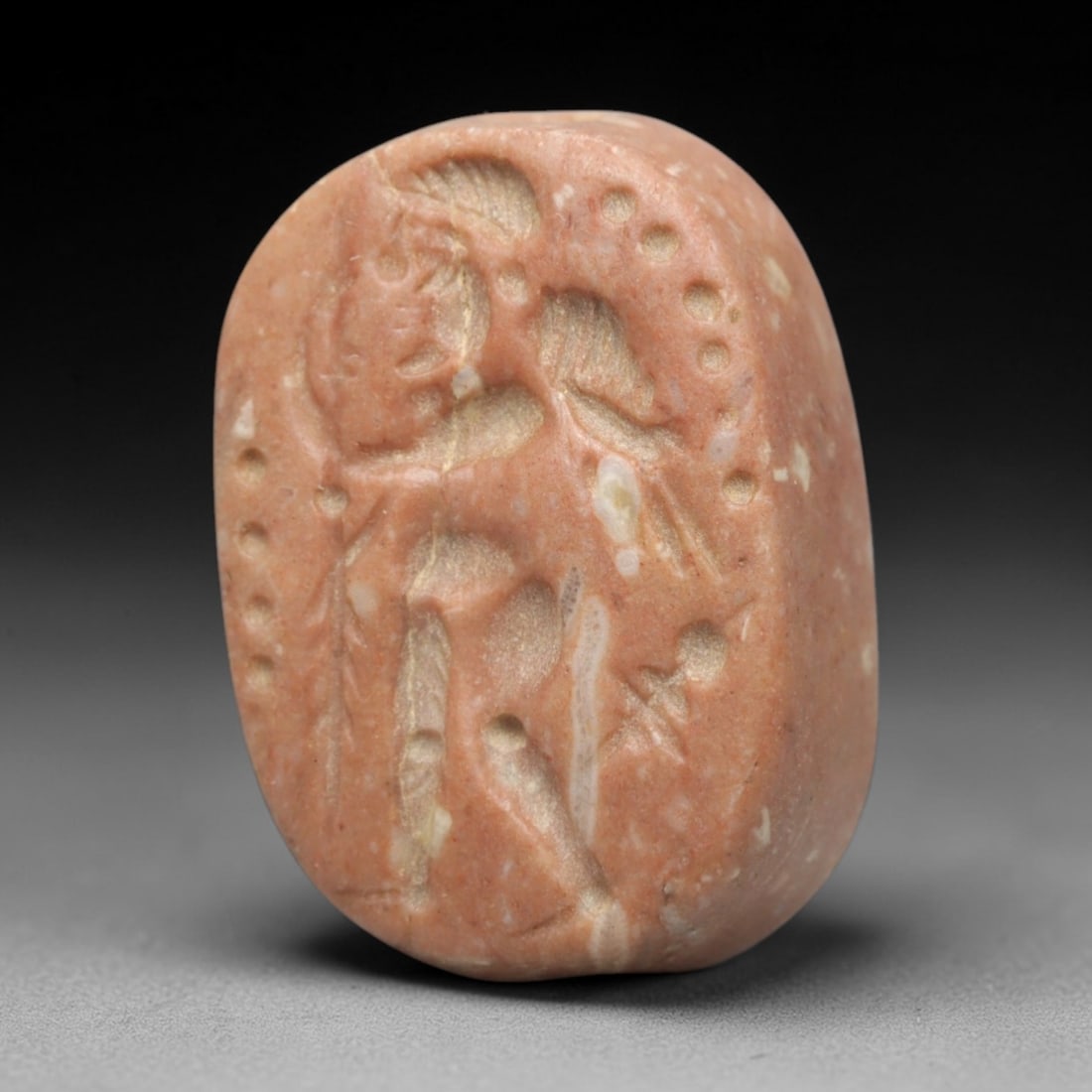 Ancient Stone Hemispherical Stamp Seal - Near Eastern Winged Anthropomorphic Figure, 39ZS: Crafted from dense, pale pinkish stone, this hemispherical stamp seal bears incised carving of a winged anthropomorphic figure, depicted with a stylized headdress, defined facial features, outstretche